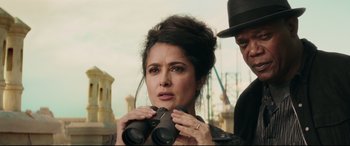 Movie still from “Hitman's Wife's Bodyguard” (2021), directed by Patrick Hughes – A woman holding a pair of binoculars while standing next to a man wearing a hat; Close Up shot, Over the shoulder angle