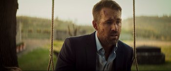 Movie still from “Hitman's Wife's Bodyguard” (2021), directed by Patrick Hughes – A person wearing a suit on a swing; Close Up shot, Over the shoulder angle