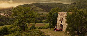 Movie still from “Hitman's Wife's Bodyguard” (2021), directed by Patrick Hughes – An image of a man standing next to a car in a field near a house; Extreme Wide shot, Low angle