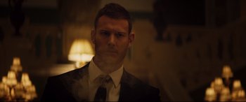 Movie still from “Hitman's Wife's Bodyguard” (2021), directed by Patrick Hughes – A man wearing a suit and tie in front of a lamp; Close Up shot, Low angle