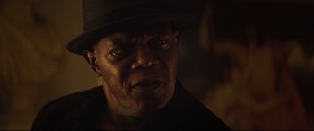 Movie still from “Hitman's Wife's Bodyguard” (2021), directed by Patrick Hughes – A person wearing a hat and looking at the camera; Close Up shot, Over the shoulder angle