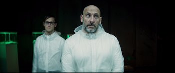 Movie still from “Hitman's Wife's Bodyguard” (2021), directed by Patrick Hughes – A bald man in a white jacket looking up; Medium shot, Low angle