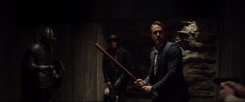 Movie still from “Hitman's Wife's Bodyguard” (2021), directed by Patrick Hughes – A man holding a baseball bat next to another man in a suit; Medium shot, Over the shoulder angle