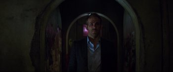 Movie still from “Hitman's Wife's Bodyguard” (2021), directed by Patrick Hughes – A man in a suit standing in a dark room; Close Up shot, Over the shoulder angle