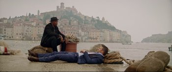 Movie still from “Hitman's Wife's Bodyguard” (2021), directed by Patrick Hughes – A man in a suit laying on the ground next to another man in a hat; Wide shot, Low angle