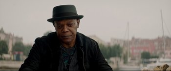 Movie still from “Hitman's Wife's Bodyguard” (2021), directed by Patrick Hughes – An older man wearing a green hat and a black jacket; Close Up shot, Low angle