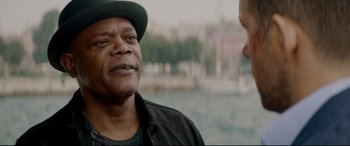 Movie still from “Hitman's Wife's Bodyguard” (2021), directed by Patrick Hughes – A man wearing a hat talking to another man in front of a body of water; Close Up shot, Over the shoulder angle