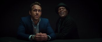 Movie still from “Hitman's Wife's Bodyguard” (2021), directed by Patrick Hughes – Two men sitting next to each other in a dark room; Close Up shot, Over the shoulder angle