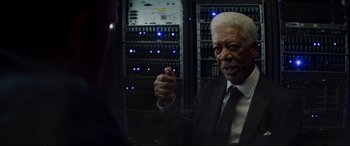 Movie still from “Hitman's Wife's Bodyguard” (2021), directed by Patrick Hughes – An older man wearing a suit and tie in front of a bunch of computers; Close Up shot, Over the shoulder angle