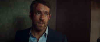 Movie still from “Hitman's Wife's Bodyguard” (2021), directed by Patrick Hughes – A person wearing a suit with blood all over his face; Close Up shot, Over the shoulder angle