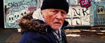 Movie still from “Hobo with a Shotgun” (2011), directed by Jason Eisener – An older man wearing a black hat and a black jacket; Close Up shot, Low angle
