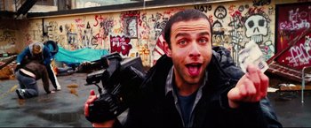 Movie still from “Hobo with a Shotgun” (2011), directed by Jason Eisener – A young man is holding a video camera in front of a graffiti wall; Close Up shot, Low angle