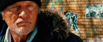 Movie still from “Hobo with a Shotgun” (2011), directed by Jason Eisener – An old man wearing a black jacket and a fur hat; Close Up shot, Low angle