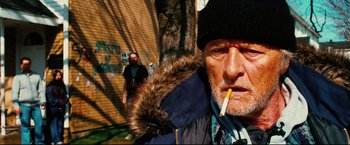 Movie still from “Hobo with a Shotgun” (2011), directed by Jason Eisener – An older man smoking a cigarette in front of a building; Close Up shot, Low angle