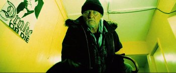 Movie still from “Hobo with a Shotgun” (2011), directed by Jason Eisener – An old man wearing a winter coat and a hat; Medium shot, Low angle