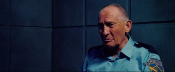 Movie still from “Hobo with a Shotgun” (2011), directed by Jason Eisener – An older man wearing a blue shirt looking at the camera; Close Up shot, Over the shoulder angle