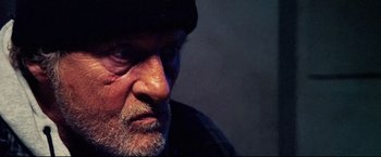 Movie still from “Hobo with a Shotgun” (2011), directed by Jason Eisener – An older man with a beard and a hat; Close Up shot, Over the shoulder angle