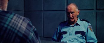 Movie still from “Hobo with a Shotgun” (2011), directed by Jason Eisener – An older man sitting in a chair in front of a brick wall; Close Up shot, Over the shoulder angle