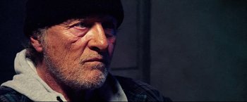 Movie still from “Hobo with a Shotgun” (2011), directed by Jason Eisener – An old man with a beard wearing a hat; Close Up shot, Low angle