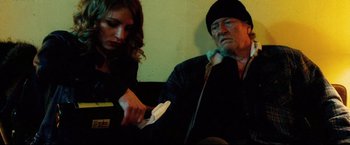 Movie still from “Hobo with a Shotgun” (2011), directed by Jason Eisener – A man and a woman sitting next to each other; Medium shot, Low angle