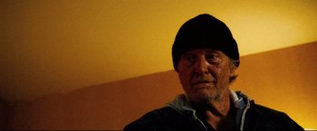 Movie still from “Hobo with a Shotgun” (2011), directed by Jason Eisener – An older man wearing a black hat in a room; Close Up shot, Low angle