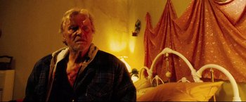 Movie still from “Hobo with a Shotgun” (2011), directed by Jason Eisener – An old man with a bloody face standing in front of a bed; Close Up shot, Low angle
