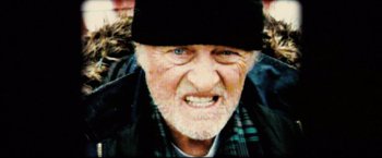 Movie still from “Hobo with a Shotgun” (2011), directed by Jason Eisener – An old man wearing a black hat and a plaid shirt; Extreme Close Up shot, High angle