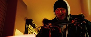 Movie still from “Hobo with a Shotgun” (2011), directed by Jason Eisener – A man smiles while holding a pipe in his hand; Close Up shot, Low angle