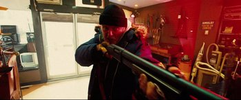 Movie still from “Hobo with a Shotgun” (2011), directed by Jason Eisener – A man is holding a rifle in a room; Medium shot, Low angle