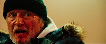Movie still from “Hobo with a Shotgun” (2011), directed by Jason Eisener – An older man wearing a green hat and a green jacket; Extreme Close Up shot, Low angle