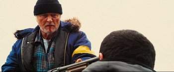Movie still from “Hobo with a Shotgun” (2011), directed by Jason Eisener – An older man wearing a winter coat and a hat; Medium shot, Over the shoulder angle