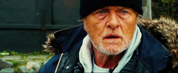 Movie still from “Hobo with a Shotgun” (2011), directed by Jason Eisener – An old man with a beard wearing a black hat; Close Up shot, Low angle