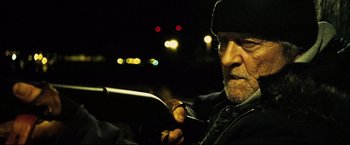 Movie still from “Hobo with a Shotgun” (2011), directed by Jason Eisener – An older man with a beard is holding a cigarette; Close Up shot, Low angle
