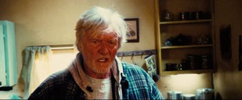 Movie still from “Hobo with a Shotgun” (2011), directed by Jason Eisener – An old man with a white beard and a blue plaid shirt; Close Up shot, Over the shoulder angle