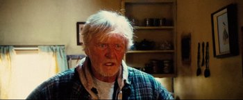 Movie still from “Hobo with a Shotgun” (2011), directed by Jason Eisener – An older man with white hair is looking at the camera; Close Up shot, Over the shoulder angle
