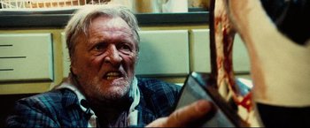 Movie still from “Hobo with a Shotgun” (2011), directed by Jason Eisener – An old man is looking into a mirror; Close Up shot, Over the shoulder angle