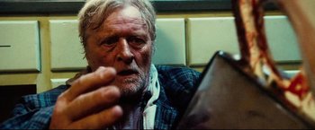 Movie still from “Hobo with a Shotgun” (2011), directed by Jason Eisener – An old man sitting in front of a phone; Close Up shot, Low angle