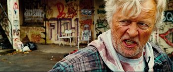 Movie still from “Hobo with a Shotgun” (2011), directed by Jason Eisener – An old man with a beard and a plaid jacket; Close Up shot, Low angle
