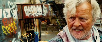 Movie still from “Hobo with a Shotgun” (2011), directed by Jason Eisener – An older woman is sitting in front of a building; Close Up shot, Over the shoulder angle