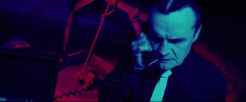 Movie still from “Hobo with a Shotgun” (2011), directed by Jason Eisener – A man talking on a phone in a dark room; Medium shot, High angle