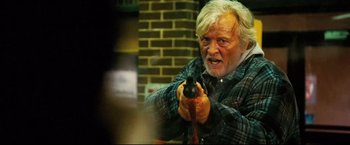 Movie still from “Hobo with a Shotgun” (2011), directed by Jason Eisener – An older man holding a gun in his hand; Medium shot, Over the shoulder angle