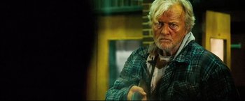 Movie still from “Hobo with a Shotgun” (2011), directed by Jason Eisener – An old man with white hair and wearing a plaid shirt; Medium shot, Over the shoulder angle