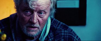 Movie still from “Hobo with a Shotgun” (2011), directed by Jason Eisener – An old man with a beard and blue eyes stares at the camera; Close Up shot, Over the shoulder angle