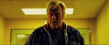 Movie still from “Hobo with a Shotgun” (2011), directed by Jason Eisener – An older man with a beard and a plaid shirt; Close Up shot, Low angle
