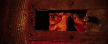 Movie still from “Hobo with a Shotgun” (2011), directed by Jason Eisener – A man's face is seen through a hole in a metal fence; Extreme Close Up shot, Overhead angle