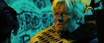 Movie still from “Hobo with a Shotgun” (2011), directed by Jason Eisener – An old man with a beard and a white beard is looking at the camera; Close Up shot, High angle