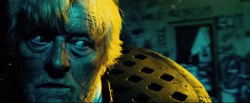 Movie still from “Hobo with a Shotgun” (2011), directed by Jason Eisener – An old man with yellow hair and blue eyes stares at the camera; Extreme Close Up shot, Overhead angle