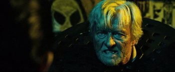 Movie still from “Hobo with a Shotgun” (2011), directed by Jason Eisener – An old man with a white beard is looking at the camera; Close Up shot, Over the shoulder angle