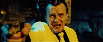 Movie still from “Hobo with a Shotgun” (2011), directed by Jason Eisener – An older man in a yellow jacket and a black tie; Close Up shot, Low angle