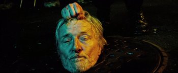 Movie still from “Hobo with a Shotgun” (2011), directed by Jason Eisener – An old man with a beard is getting his head shaved; Close Up shot, Overhead angle